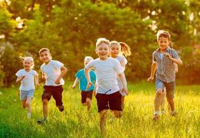 un grupo de niños felices de niños y niñas corren en el parque sobre el césped en un día soleado de verano. foto