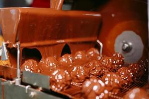 Sweets production and industry concept - chocolate candies processing on conveyor at confectionery shop. photo