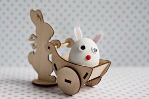 A wooden rabbit carries a cart with an egg with bunny ears. Easter decorations