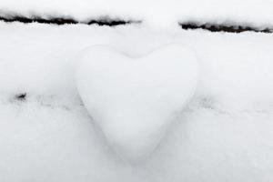 un corazón blanco como la nieve hecho de nieve en un banco. el concepto del dia de san valentin
