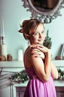 A young girl in a pink dress on the background of Christmas decorations and a fireplace in the room photo