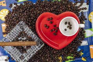 Composición de granos de café con taza y platillo en forma de corazón foto