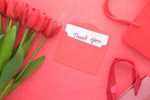 Thank you message on paper with tulip flower on red background photo