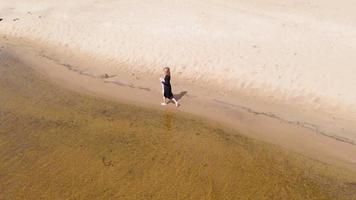 una mujer joven con un vestido corre a lo largo de la toma aérea de la playa