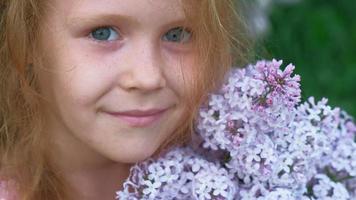 une petite fille à l'extérieur dans un parc ou un jardin détient des fleurs lilas buissons lilas en arrière-plan parc d'été
