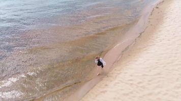 una mujer joven con un vestido corre a lo largo de la toma aérea de la playa