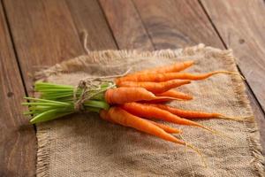 zanahorias frescas frescas sobre tabla de cortar de madera y fondo de madera foto