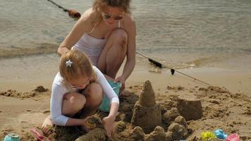 Mutter und Tochter spielen am Strand und bauen eine Sandburg