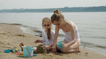 Mutter und Tochter spielen am Strand und bauen eine Sandburg