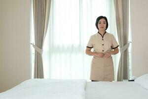 Young Asian chambermaid in the hotel room looking at camera photo