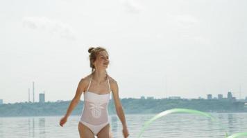gimnasta joven vistiendo un traje blanco en una playa de arena, bailando con cinta de gimnasia.