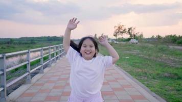 menina asiática correndo na pista com uma cara sorridente e acenando para a câmera video