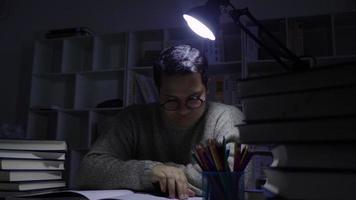 Stressed Asian man sitting on a chair reading book at night in a dark room video