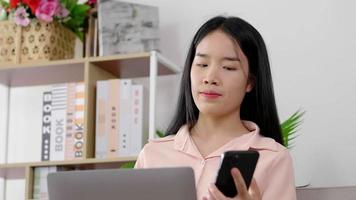 Aziatische vrouw die op laptop werkt en met een vriend praat op smartphone video