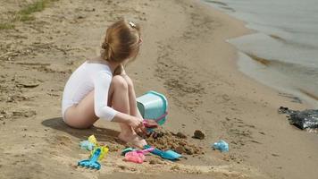 Girl child plays with sand on the beach using molds figurines Sunny summer day vacation video