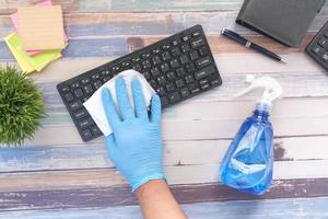Mano en guantes de goma azul y teclado desinfectante de tejido blanco foto
