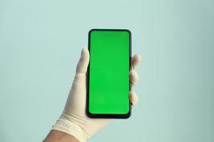 Mano en guantes de látex sosteniendo un teléfono inteligente con pantalla verde foto