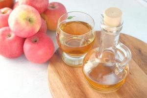 Vinagre de manzana en botella de vidrio con manzana verde fresca en la mesa foto