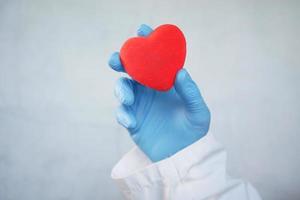 Man hand in protective gloves holding red heart on white background photo