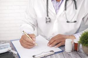 Doctor hand writing prescription on clinic desk with pill contianer on table photo