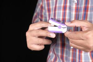 Close up of man hand using pulse oximeter isolated on black photo