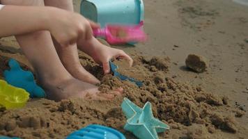 Girl child plays with sand on the beach using molds figurines Sunny summer day vacation video