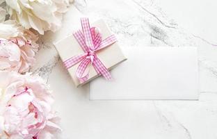 Peonías rosas con tarjeta vacía y caja de regalo sobre fondo de mármol blanco foto