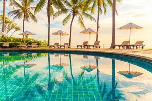 Hermosa sombrilla de lujo y una silla alrededor de la piscina al aire libre en el hotel y resort con palmera de coco en el cielo al atardecer o al amanecer