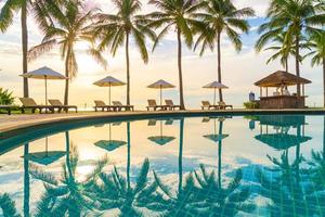 Hermosa sombrilla de lujo y una silla alrededor de la piscina al aire libre en el hotel y resort con palmera de coco en el cielo al atardecer o al amanecer