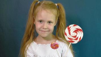 Little girl with a lollipop on a blue background Close up portrait