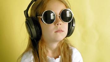 petite fille joyeuse dans les écouteurs sur fond jaune closeup portrait video