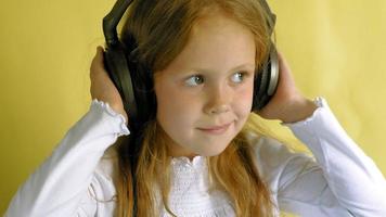 Cheerful little girl in headphones on a yellow background Closeup portrait video