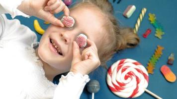Cheerful little girl lies on a blue background with sweets Closeup portrait video