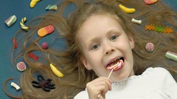 Little girl with a lollipop lies on a blue background Closeup portrait top view