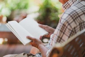 Senior hombre jubilado asiático sentado en un banco y libro de lectura en el patio de casa durante el tiempo libre