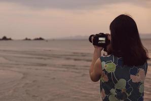 Portrait of young woman using camera to take picture of the beach during summer vacation photo