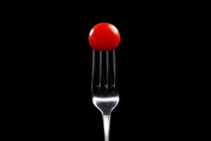 Fork with cherry tomato close-up. Isolated image on a black background. Macro photo. cooking concept photo