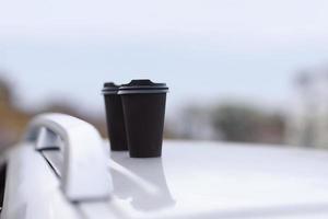 Dos vasos negros de bebidas en un stand sobre un fondo borroso de la ciudad. café o té para llevar en vasos desechables. un refrigerio rápido. tazas de café en el coche. enfoque selectivo foto