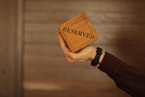 A wooden plaque has a word reserved . male hand holds a wooden plate with the inscription reserved isolated on a white background. selective focus. photo