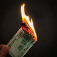 The hand holds a burning hundred dollars. Illustration of the financial crisis and loss of money and capital. photo