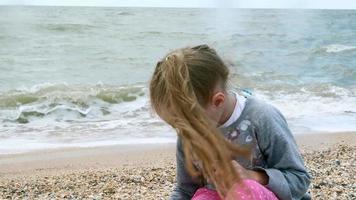 klein meisje op het zeestrand verzamelt schelpen zomer video