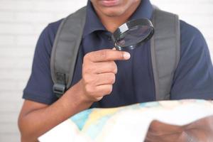 young man using magnifying glass looking something on map photo