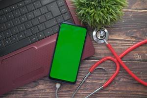 Medical Stethoscope and smart phone on laptop on wooden table photo