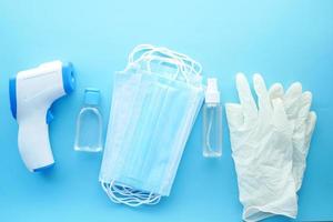 Surgical masks, thermometer and hand sanitizer on blue background . photo