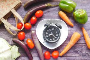 fresh vegetables and alarm clock on heart shape plate on table photo