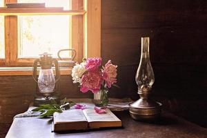 Bodegón de artículos vintage y un ramo de peonías en una mesa junto a la ventana. foto