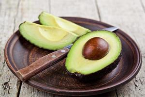 Aguacate orgánico fresco en plato de cerámica y cuchillo sobre fondo de mesa de madera rústica. foto