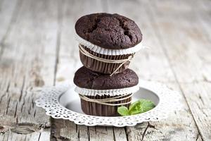 Two fresh dark chocolate muffins with mint leaves on white plate on rustic wooden table photo