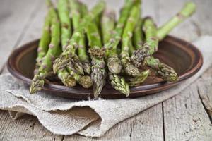 Fresh raw garden asparagus closeup on brown ceramic plate and linen napkin on rustic wooden table background. photo