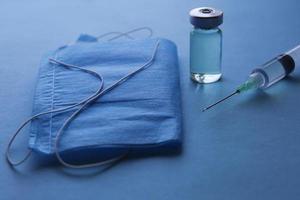 glass bottle with medicine, syringe and disposable mask on the blue surface photo